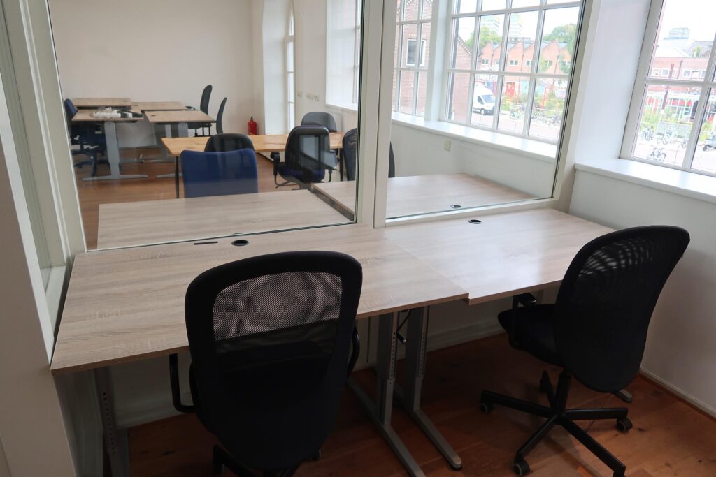Twee werkplekken met bureaustoelen gescheiden door een glazen wand in een lichte kantoorruimte aan het Gedempt Hamerkanaal.